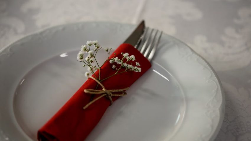 Elegant table setting with a red napkin, cutlery, and white flowers for a classy dining experience.